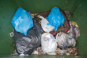 Milan, Italy - December 02, 2019: selective waste collection bins, big green dumpster full of garbage bags,Undifferentiated waste collection