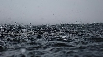 Rain drops into the endless ocean, close up. It briefly bounces back to the air after it hits the sea surface, slow motion.