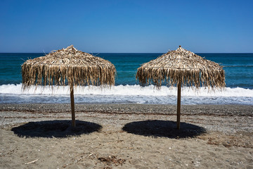 Beach umbrellas made of palm leaves on the beach of the Aegean Sea in Greece.