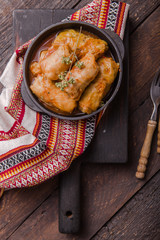 Meat in cabbage rolls in a black pan with  sauce on wooden background.  Asian cuisine top view