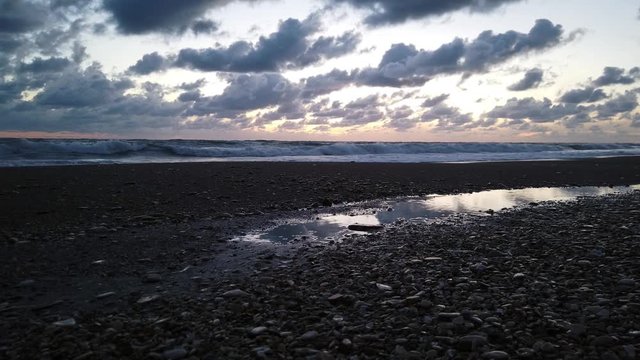 Amazing low angle view at blue hour sunset from the pebbles beach to the horizon with dramatic lights reflections on the water and beautiful blue color pastel sky with dark cirrocumulus clouds