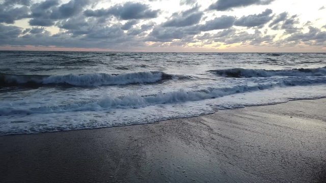 Low angle view at blue hour sunset from the beach to horizon  with dramatic lights and amazing undertow movement, white foam of waves crashing on the sand in a beautiful blue color pastel sky with dar