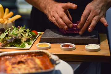 Hands placing raw steak on the hot stone