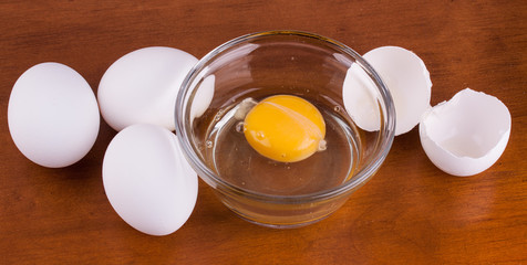 Broken egg in a glass bowl with whole eggs and shell