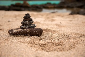 Fototapeta na wymiar Piedras marrones volcánicas sobre arena amarilla de playa en equilibrio y fondo de mar