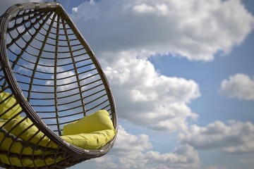 Clouds on a blue sky and a round rattan swing on a chain.  The concept of a carefree summer holiday on a sunny day. Dreams of a summer vacation. bright summer background for website design, poster.