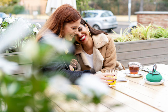 Two happy female friends drinking tea outdoors at a coffee shop