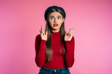 Attractive woman with long hair praying and crosses her fingers over red background. Pretty girl begging someone. Hope concept.