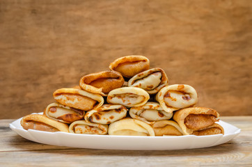 Pancakes with filling stacked pyramid on a white plate, standing on a wooden background close-up