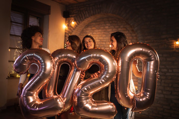 Girlfriends celebrating New Years Eve holding 2020 balloons