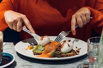 Young woman in orange sweater eating poached eggs on toast