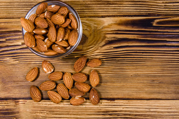 Glass bowl with the peeled almond nuts on wooden table. Top view