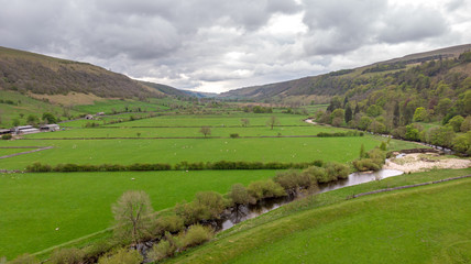 Obraz premium An aerial view of a mountain valley with green pasture, farm, river and trees under a stormy sky