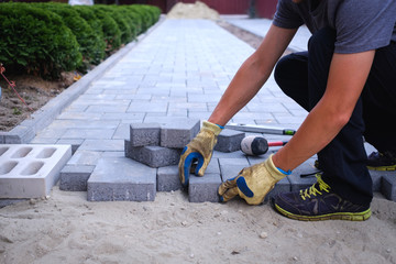 The master in yellow gloves lays paving stones