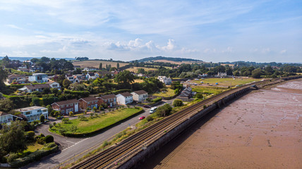 An aerial view of a railway track dam along a sandy beach, road and building area under a majestic cloudy blue sky