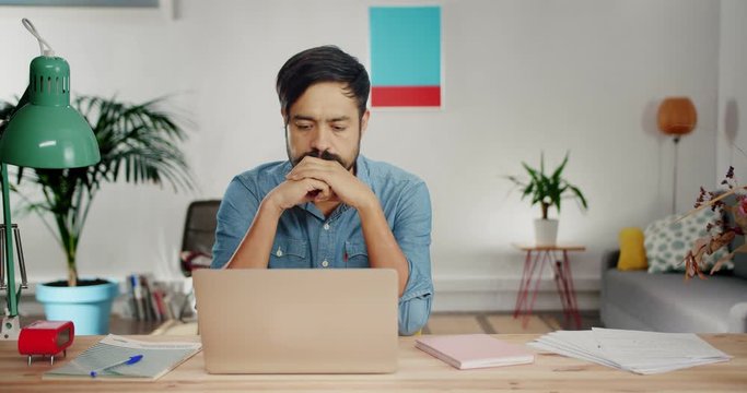Disappointed Hispanic man feeling angry and funny expressing anger at modern home office, sorrowful young male dressed in casual jeans shirt can not concentrate on work because of domestic sad problem
