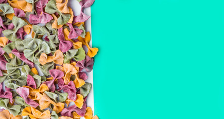 Pile of Italian dried Tri Color Farfalle pasta. Various colors of bow tie on trendy green mint color background
