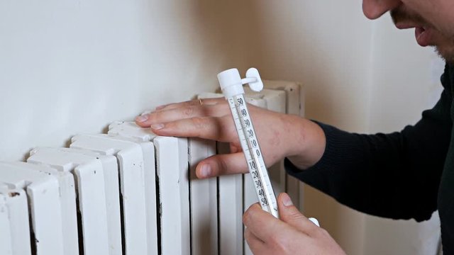 Man checking the temperature of the heating battery. Cold winter, cold in the house, apartment. A man warms himself near a heating battery