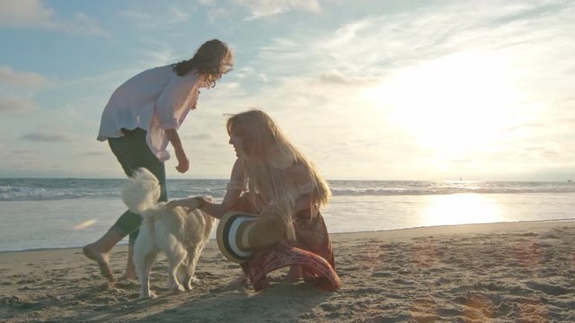 Slow motion of mother and teenage daughter playing with their dog by the ocean