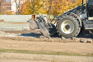A tractor with a bucket performs construction work on cleaning the territory at a construction site.