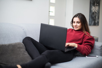 Fototapeta premium Woman using a laptop while relaxing on the couch