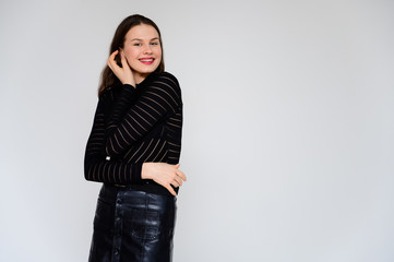 Concept adult girl on a white background. A photo of a pretty brunette girl in a black skirt and black sweater smiles and shows different emotions in different poses right in front of the camera.