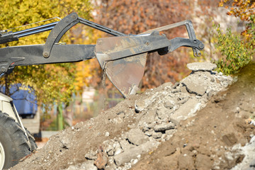 A tractor with a bucket performs construction work on cleaning the territory at a construction site.