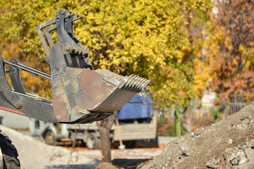 A tractor with a bucket performs construction work on cleaning the territory at a construction site.