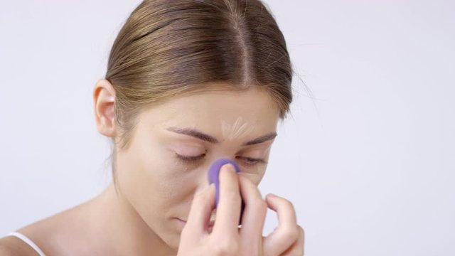 Close up shot of beautiful young woman blending her concealer with makeup sponge