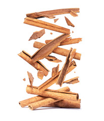 Cinnamon sticks are falling down on a pile on a white background