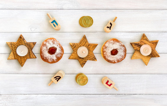 Wooden candlesticks in the shape of star, donut, golden chocolate coins and dreidels on background of white painted wooden planks. Jewish holiday Hanukkah. Top view, flat lay