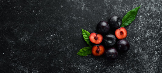 Fresh plums with leaves on a black stone table. Top view. Free space for your text.