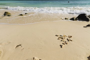 Beautiful seascape view. Shells and fancy pebbles on white sand and turquoise rolling waves on background. Atlantic ocean. 