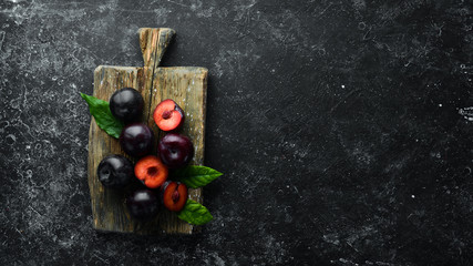 Fresh plums with leaves on a black stone table. Top view. Free space for your text.