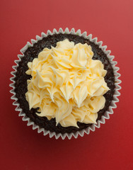 Top view of a chocolate cupcake with vanilla icing, red background