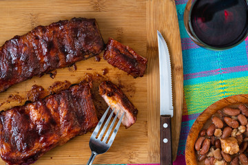 BABY BACK RIBS WITH BBQ AND BAKED BEANS WITH BACON, SERVED ON A WODDEN TABLE, AND RED WINE GLASS
