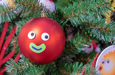 Red Christmas ball with eyes and a smile hanging on a Christmas tree.