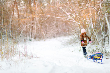 Fototapeta na wymiar A girl plays in the winter forest at sunset. Children sledding in a snowy park. Winter holiday.