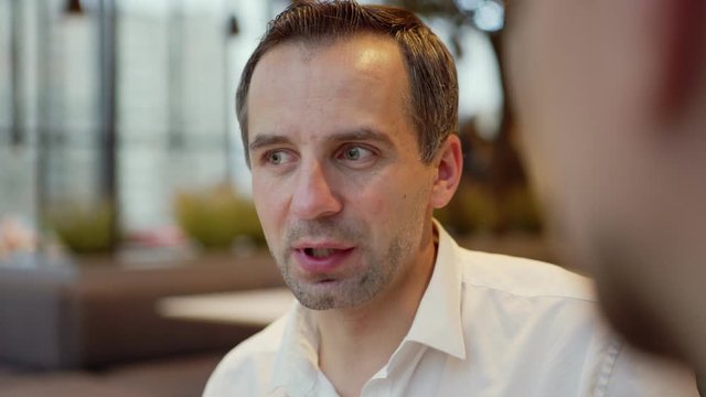 Closeup Head And Shoulders Shot Of Middle Aged Businessman Talking To Unrecognizable Business Partner Sitting In Cafe