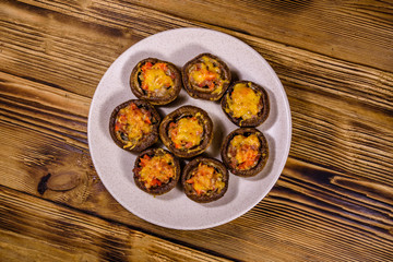 Fototapeta na wymiar Baked champignons stuffed with minced meat and cheese in plate on a wooden table. Top view