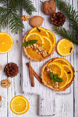 Obraz na płótnie Canvas Mini tart pies with orange, custard cream and walnuts on wooden background. Sweet Christmas dessert. 