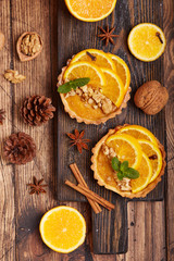 Mini tart pies with orange, custard cream and walnuts on wooden background. Sweet Christmas dessert. 