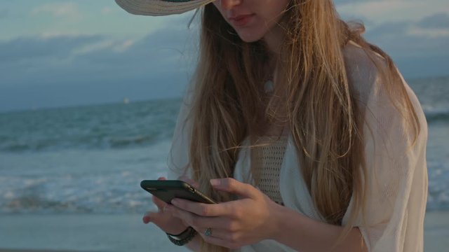 Young woman at the beach scrolling on her cellphone