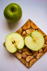 Tasty food in green. Two apples: one is whole, the other cut into two parts. Broccoli in a strange pyramid shape. Knife and board for cutting made of wood.