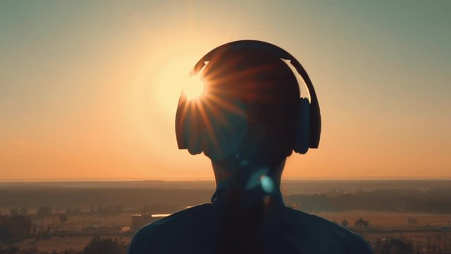 b roll female enjoy music outdoors slow motion listening song at sunrise warm landscape with gold rays of sun lens flare