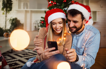 Love couple celebrating Christmas holiday at home and using phone 