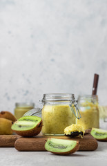 Homemade kiwi jam in a preserving glass. Exotic kiwi jam. Light grey stone background, selective focus.