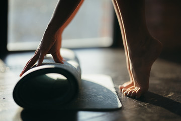 A girl rolls a rug with her hands and stands on toes on the floor for yoga in a fitness studio or at home in sunny weather