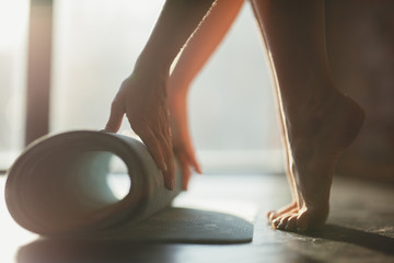 A girl rolls a rug with her hands and stands on toes on the floor for yoga in a fitness studio or at home in sunny weather
