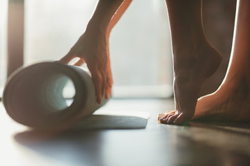 A girl rolls a rug with her hands and stands on toes on the floor for yoga in a fitness studio or at home in sunny weather